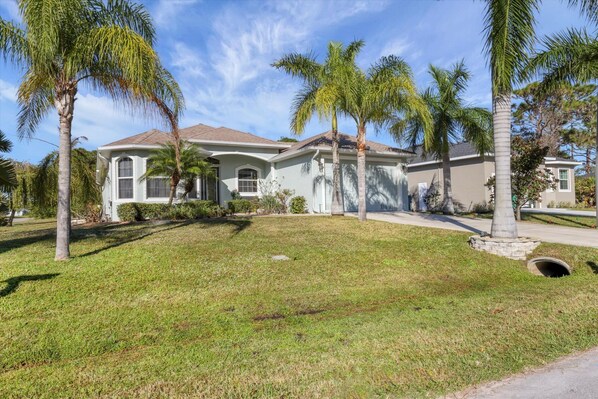 A two-story house with a front yard, palm trees, and a clear sky. - NewToVRBO RELAX- Own Home Private Pool, Hot Tub, near Beaches, Golf & Pickleball (Rotonda West)