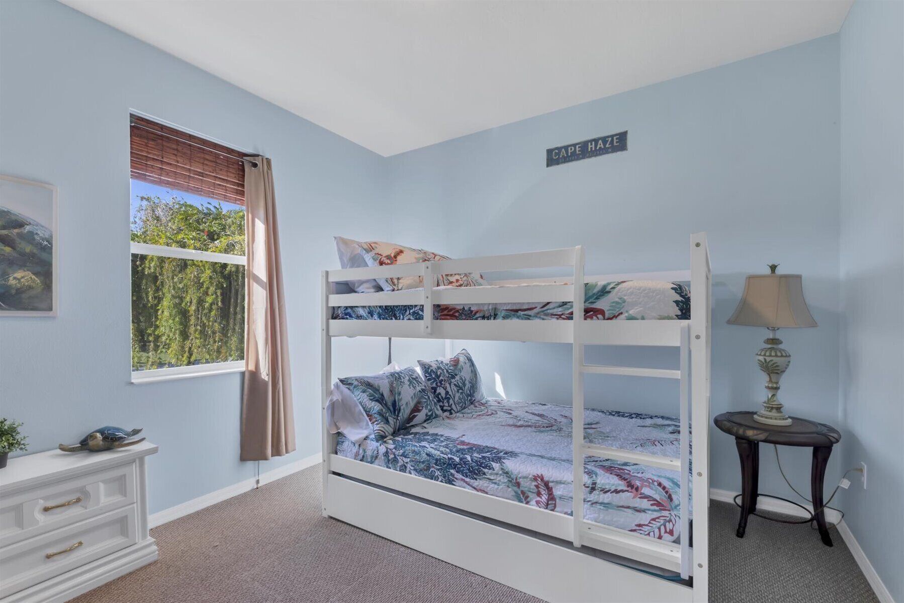 A bunk bed room with a window, a dresser, and a lamp.