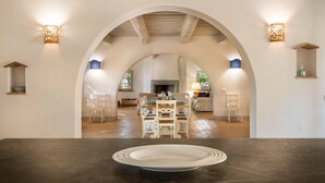 Een eetruimte met een tafel en stoelen, een keuken op de achtergrond en decoratieve wandlampen.