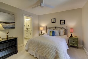 Un dormitorio con cama, mesitas de noche, cómoda, ventilador de techo y cuadros en las paredes.
