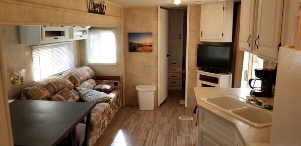 Un intérieur de camping-car compact comprenant un canapé, un coin cuisine et un téléviseur.