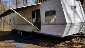 Un camping-car blanc doté d’un auvent rétractable, d’une porte coulissante et d’une fenêtre.