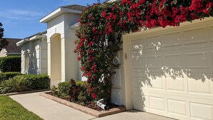 A residential garage with a white exterior and a red flowering vine climbing over the garage door.