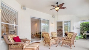 A spacious patio with wicker furniture, a ceiling fan, and a view of the interior.