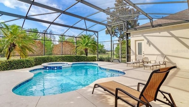 An indoor swimming pool with a glass ceiling, surrounded by lounge chairs and a landscaped garden.