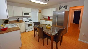 A kitchen with white cabinets, a granite countertop, a stainless steel refrigerator, and a dining table with chairs. - Home Sweet Home - Peace, Love, & Enjoy (Kingsville)