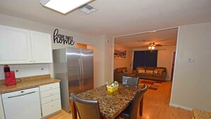 A compact kitchen with white cabinets, a stainless steel refrigerator, a dining table with four chairs, and a small coffee maker. - Home Sweet Home - Peace, Love, & Enjoy (Kingsville)