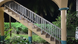 A staircase with beige steps and white balusters, surrounded by greenery and a fence.