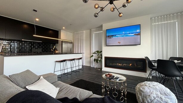 A modern living room with a sofa, a coffee table, a fireplace, a TV, and a kitchen area in the background.