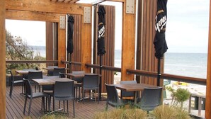 An outdoor seating area with wooden tables and chairs, overlooking the sea.
