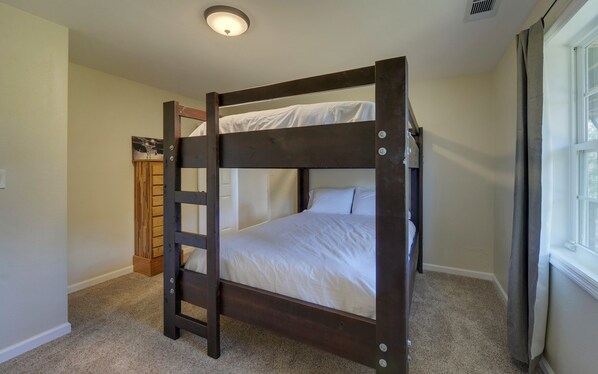 A bunk bed with a ladder, carpeted floor, and a window with curtains.