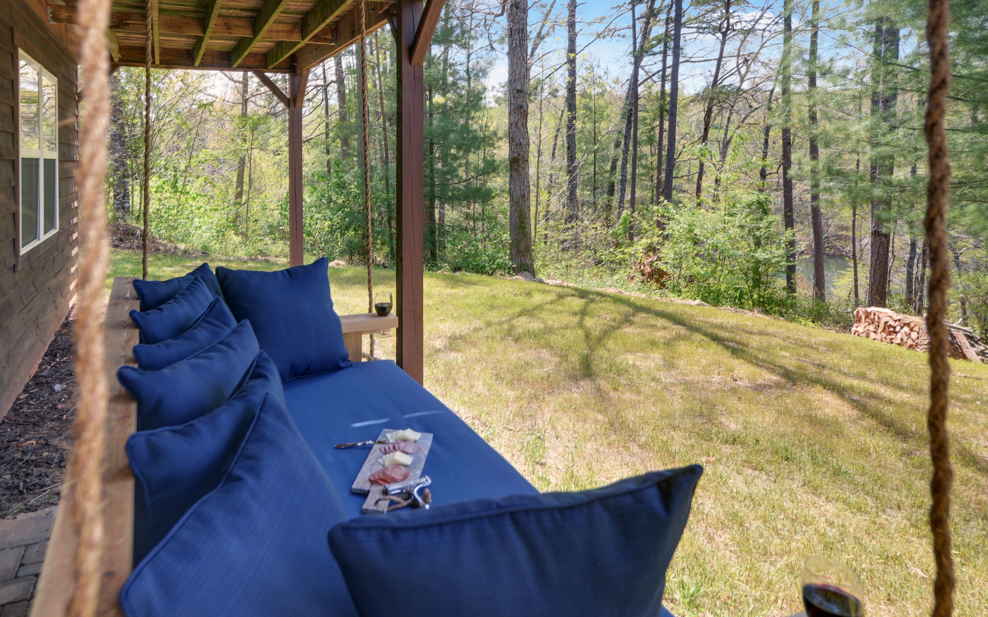 A covered outdoor seating area with blue cushions and a wooden table with a wine glass and a menu.