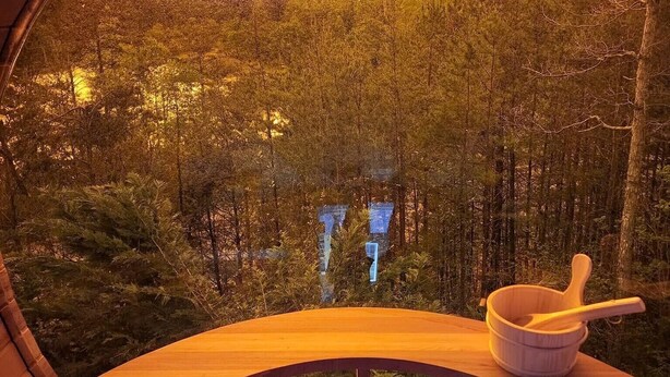 Une structure circulaire en bois, dotée d’un banc et d’un bol en bois avec une cuillère, qui offre une vue sur un paysage boisé.
