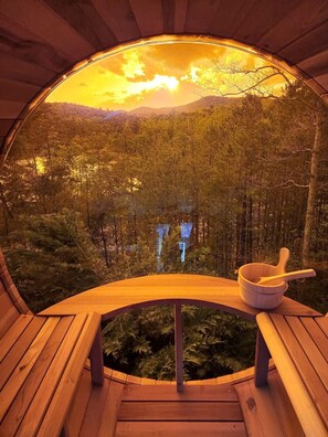 A circular wooden structure with a bench and a wooden bowl with a spoon, overlooking a forested landscape.