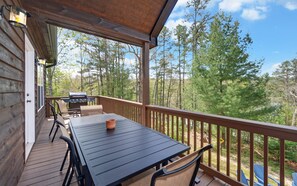 A wooden deck with a table and chairs, a barbecue grill, and a view of a forest.