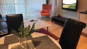 A modern living room with a white coffee table, two black leather chairs, a red armchair, a large flat-screen TV mounted on the wall, and a potted plant on the coffee table. - Apartment-sleeps4-balcony-parking-petsok (Hull)