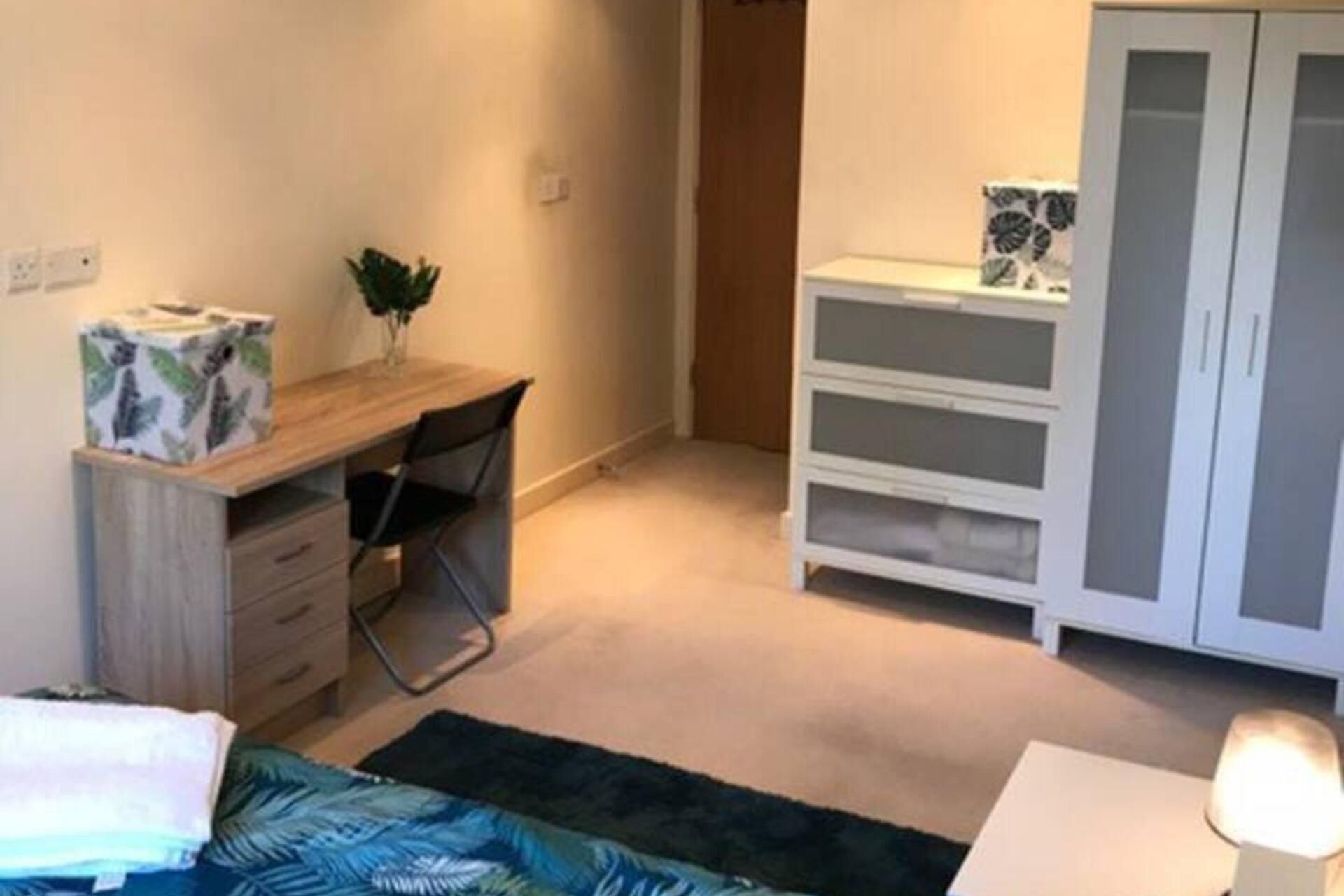Un dormitorio con cama, escritorio, silla, armario y mesita de noche.