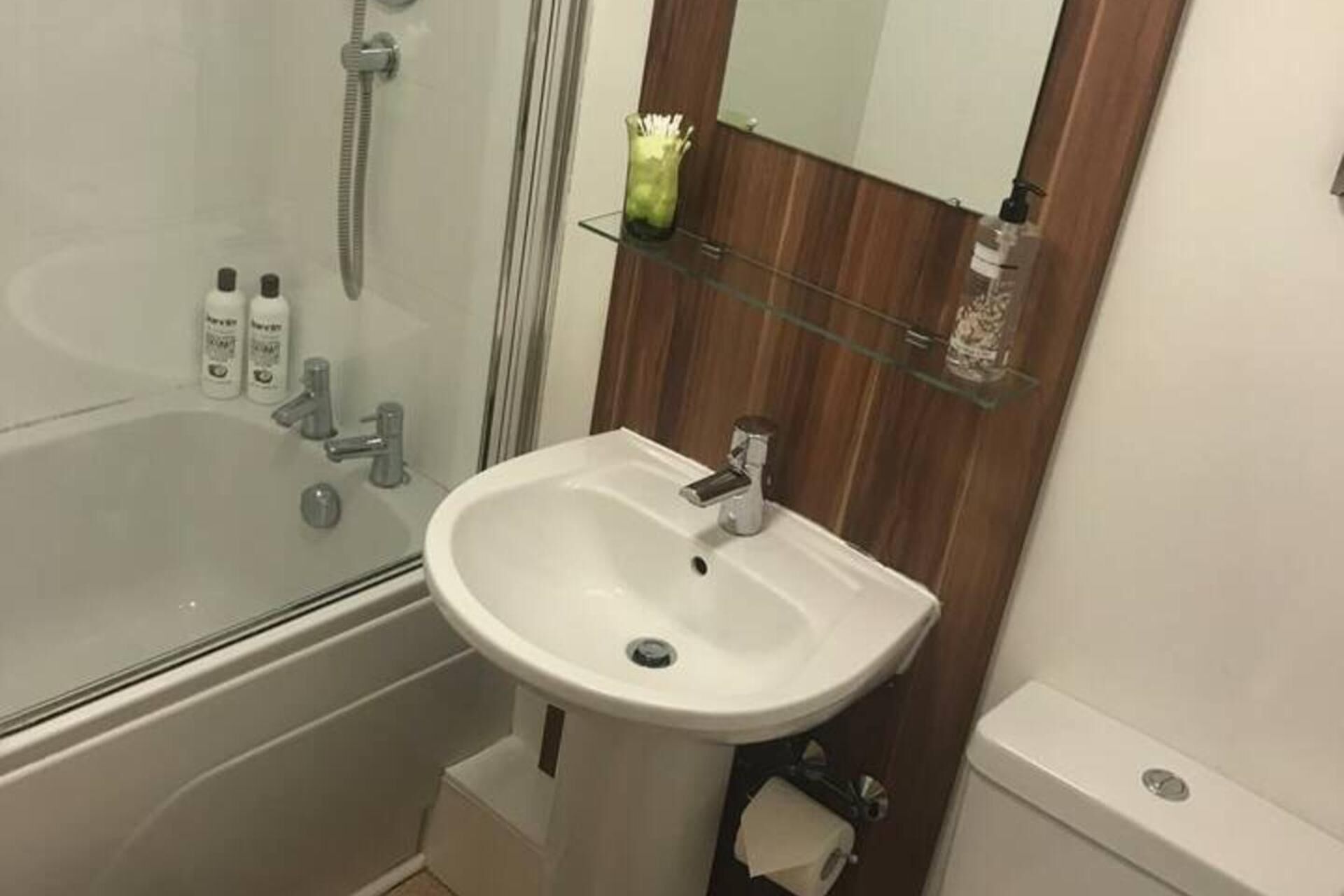 A bathroom with a white sink, a glass shower enclosure, and a wooden vanity with a mirror.