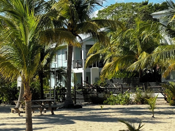 Una propiedad frente a la playa con un edificio de dos pisos, palmeras y una zona de arena.