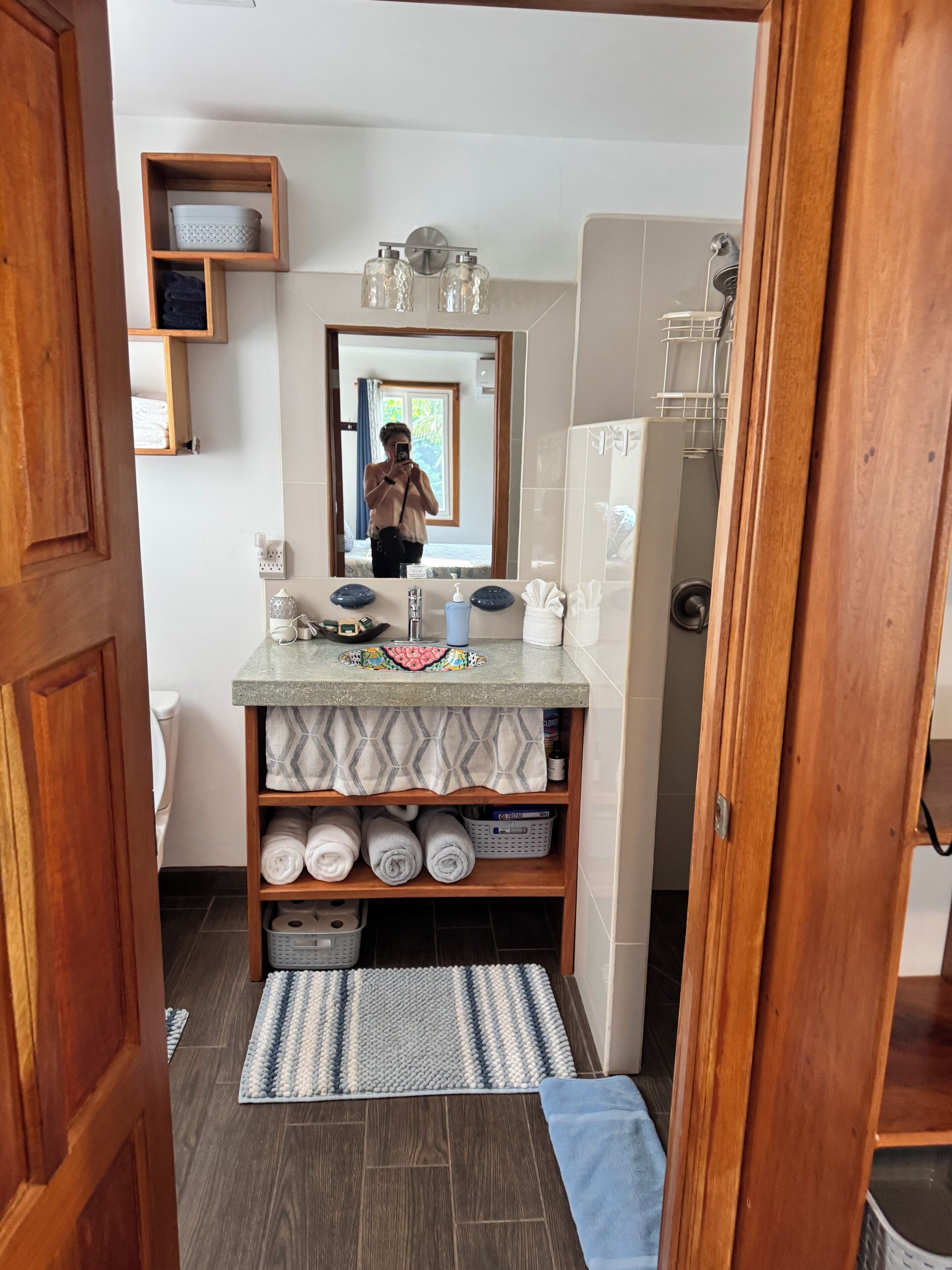 Une salle de bain avec un meuble-lavabo en bois, un miroir, un porte-serviettes et une étagère contenant des articles de toilette.