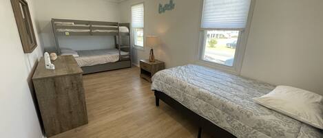 A bedroom with two bunk beds, a bedside table, a lamp, and a window with blinds.