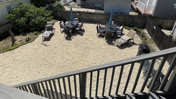 Un patio trasero con zona de arena, mobiliario exterior y una terraza de madera.