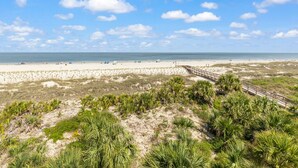 Una spiaggia con una passerella in legno, dune sabbiose e vegetazione rada.