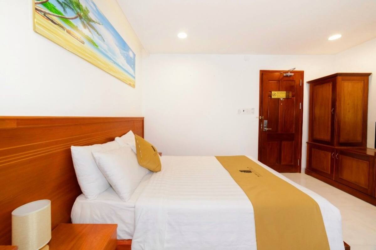 Habitación de hotel con una cama grande, cabecera de madera, un cuadro en la pared, un armario y una puerta con un cartel.