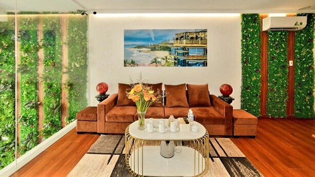 Una sala de estar moderna con un sofá marrón, una mesa de centro y un cuadro de una casa de playa en la pared.