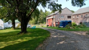 A paved path leading to a building with a red door, surrounded by greenery and a tree. - Farmstay, 2 bedrooms with 2 private baths, private entrance. (Waldoboro)