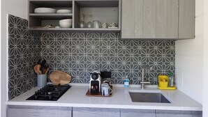 Et køkken med et mønstret backsplash, en kaffemaskine, en vask og en bordplade med redskaber.