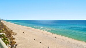 Une plage avec une jetée qui s’avance dans l’océan, un ciel dégagé et quelques personnes qui se promènent le long du rivage.