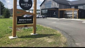 Een bord voor Lac Brôme Meer met een houten omlijsting en een logo, en een gebouw met een modern ontwerp op de achtergrond.