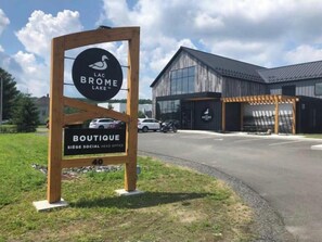 A sign for Lac Brôme Lake with a wooden frame and a logo, and a building with a modern design in the background.