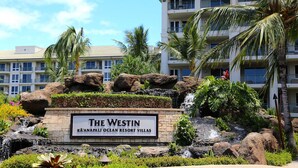 Le Westin Kona Resort Villas, avec un panneau indicateur, des palmiers, une cascade et un bâtiment en arrière-plan.