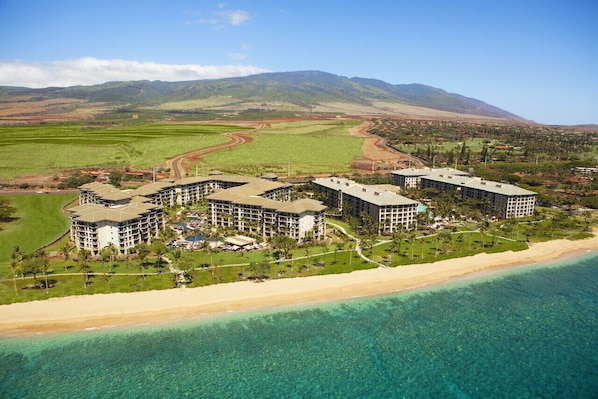 A beachfront hotel with multiple buildings, a sandy beach, and a clear view of the ocean.