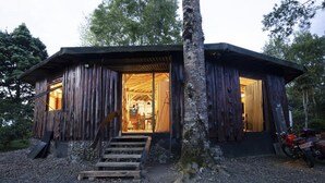 Une cabane rustique avec une façade en bois, un escalier menant à l’entrée et une moto garée à l’extérieur.