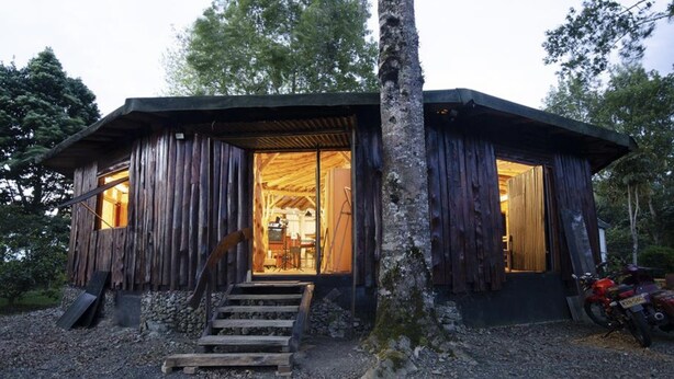 A rustic cabin with a wooden exterior, a staircase leading to the entrance, and a motorcycle parked outside. - The round house in Filandia with waterfall (Filandia)