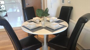Une table de salle à manger ronde, avec quatre chaises noires, des sets de table blancs et une plante en pot.
