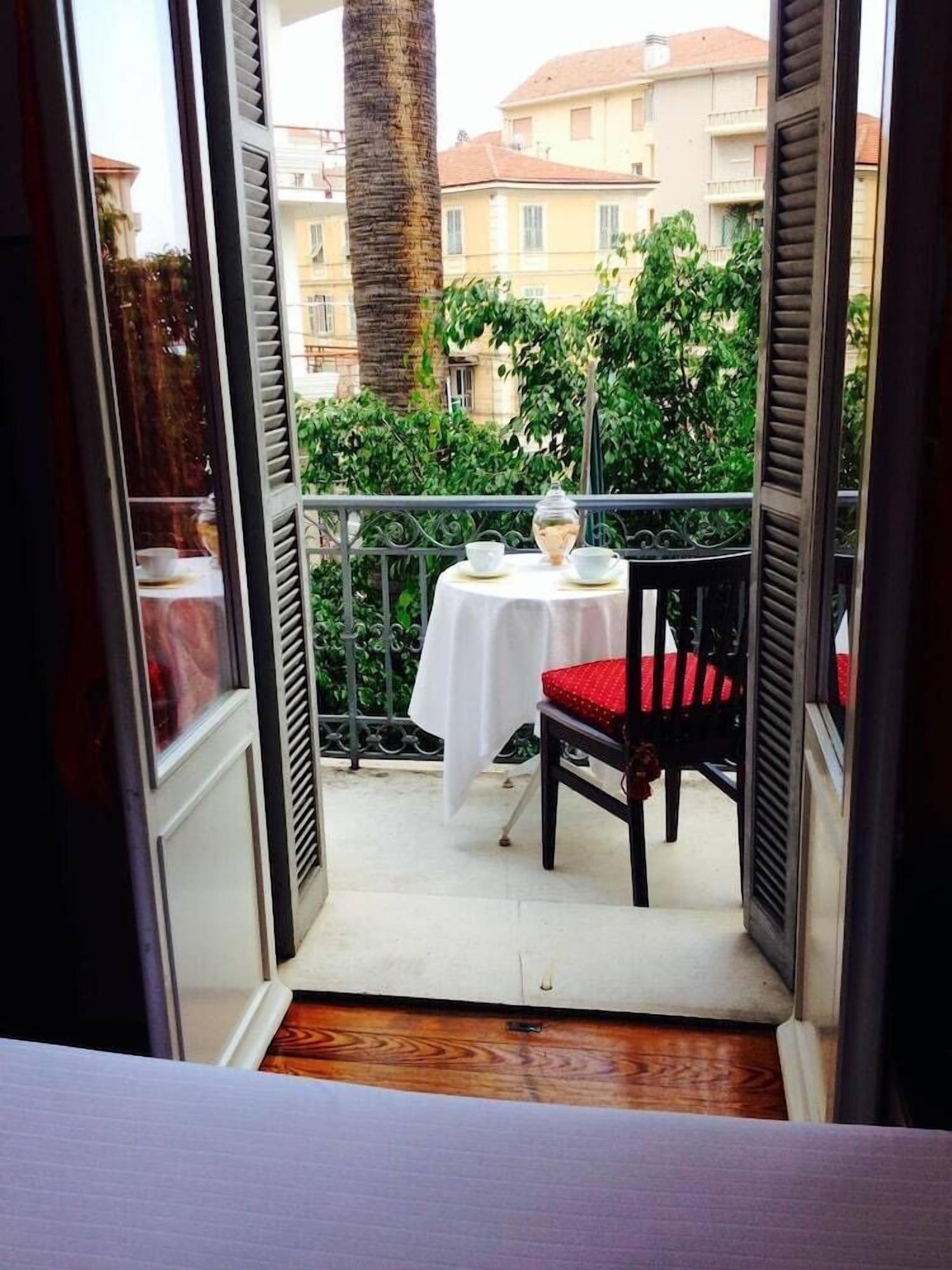 Un balcone con tavolo e sedie, vista su edifici e vegetazione sullo sfondo.