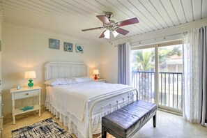Un dormitorio con cama, mesitas de noche, un banco, ventilador de techo y vistas al exterior.