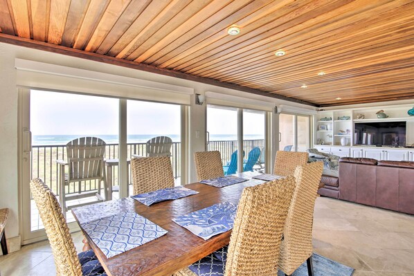 Enjoy meals with a view of the ocean from this dining area featuring a long table and wicker chairs.