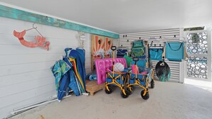 A room with a white wall, a wooden floor, and a ceiling light. There are various items on the wall, including a sign, a wooden structure, and a rack with bags. - Bluewater Beach House will not disappoint (Fort Myers Beach)