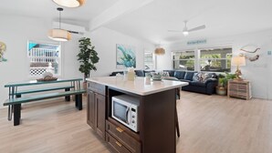 A modern kitchen with a central island, a dining area with benches, and a living room with a sofa and a ceiling fan. - Bluewater Beach House will not disappoint (Fort Myers Beach)
