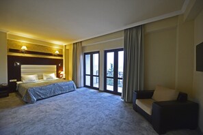 Habitación de hotel con una cama grande, un sofá, un escritorio y un balcón con vistas.