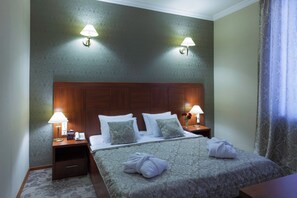 A hotel room with a large bed, two bedside lamps, a wooden headboard, a nightstand with a telephone, and a window with curtains. - Astoria Tbilisi (Tbilisi)