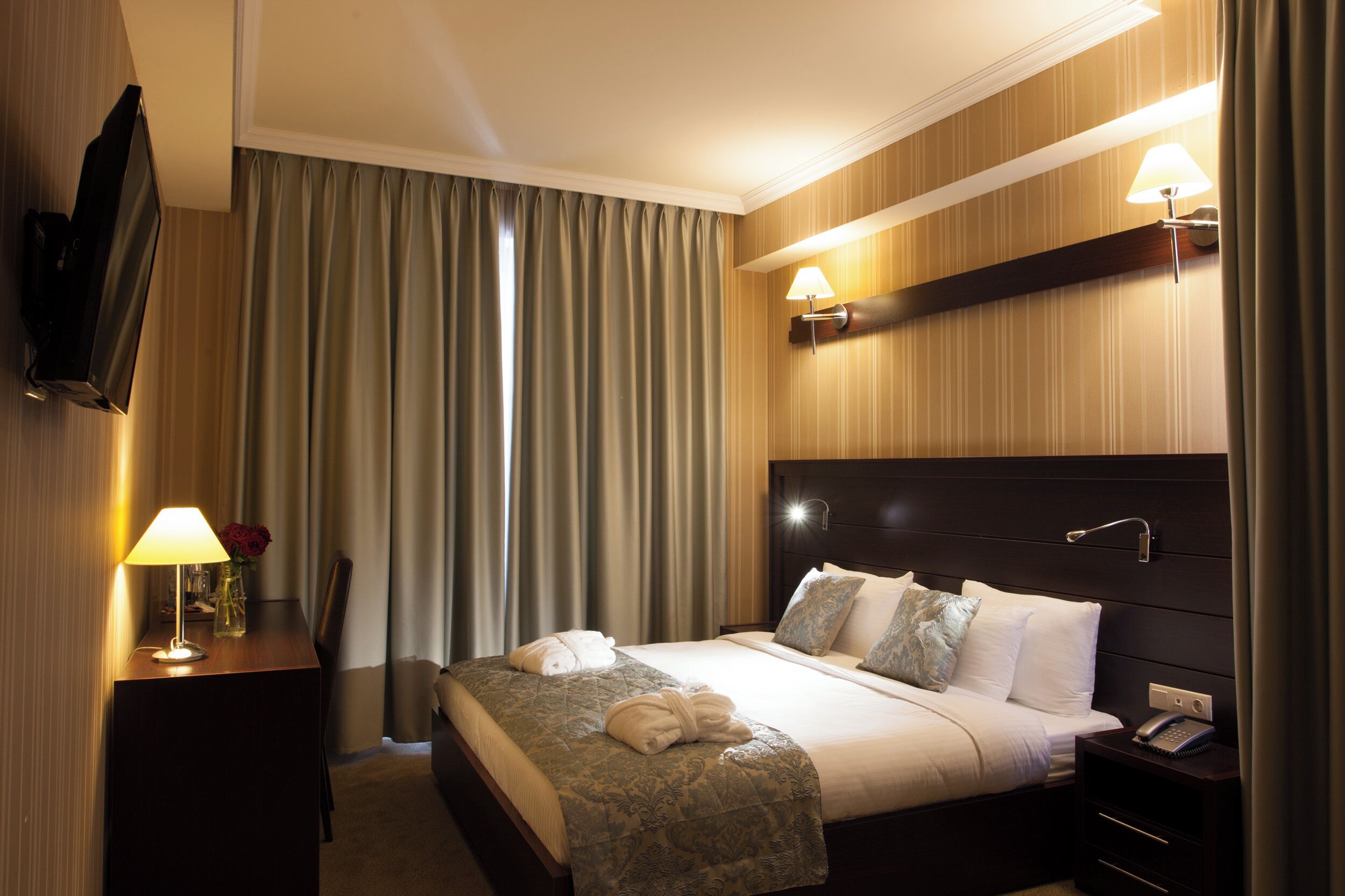 A hotel room with a bed, bedside lamp, TV, and a nightstand with a phone.