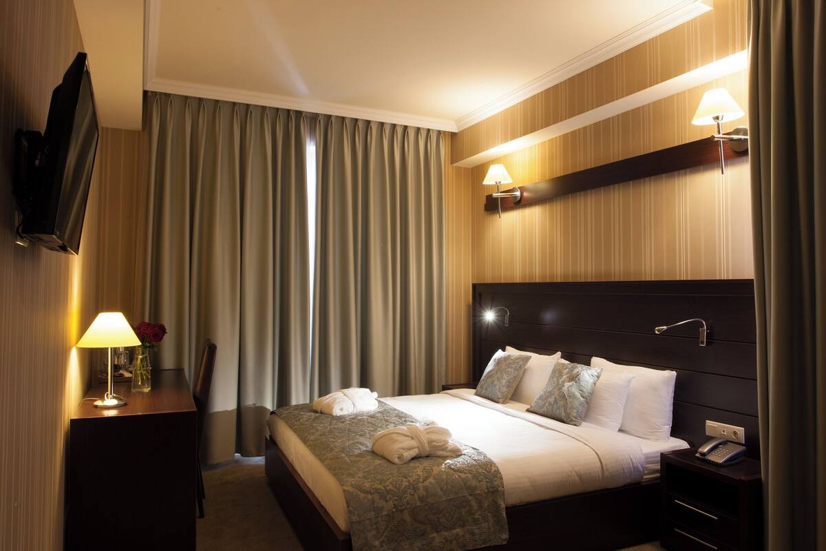 Ein Hotelzimmer mit Bett, Nachttischlampe, Fernseher und einem Nachttisch mit Telefon.