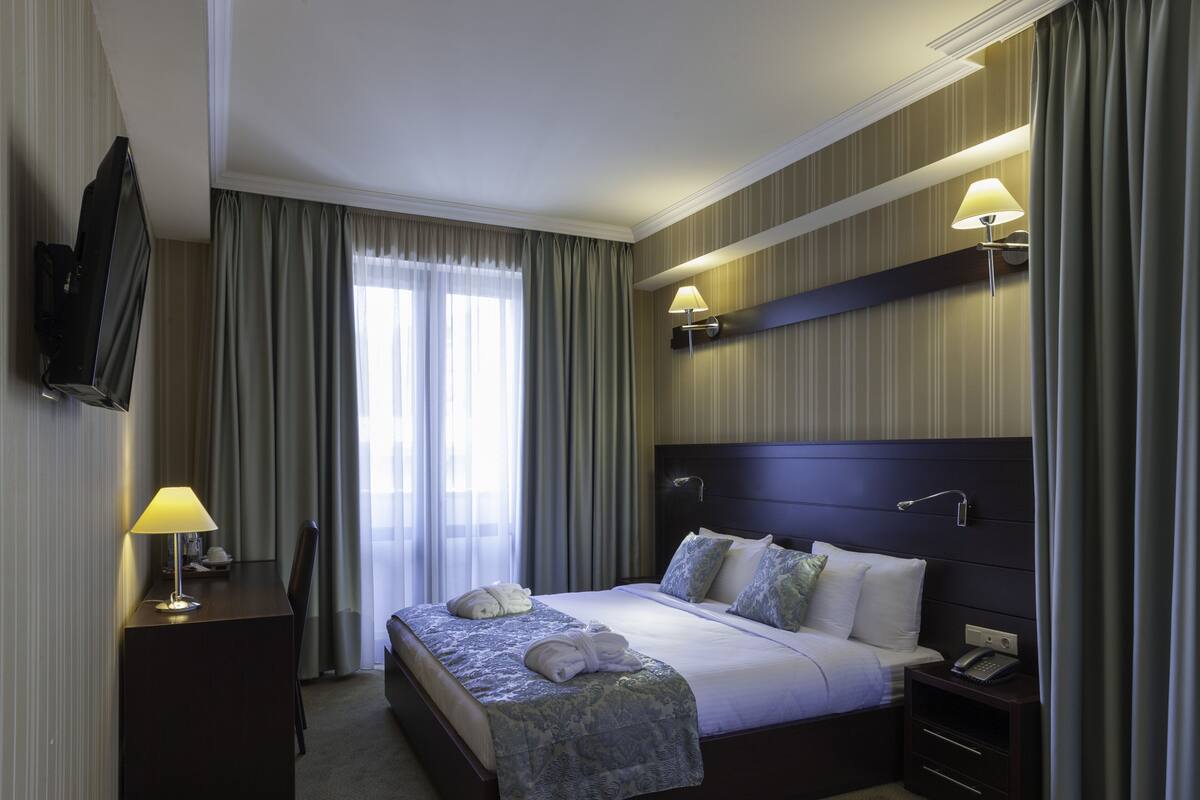 Ein Hotelzimmer mit einem Bett, Nachttischlampen, einem Fernseher und einem Schreibtisch mit Lampe.
