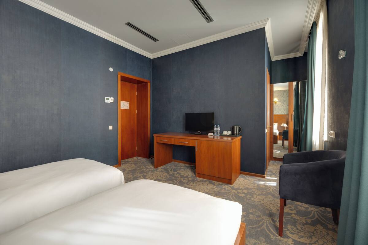 Ein Hotelzimmer mit zwei Betten, einem Schreibtisch mit Fernseher und einem Sessel.